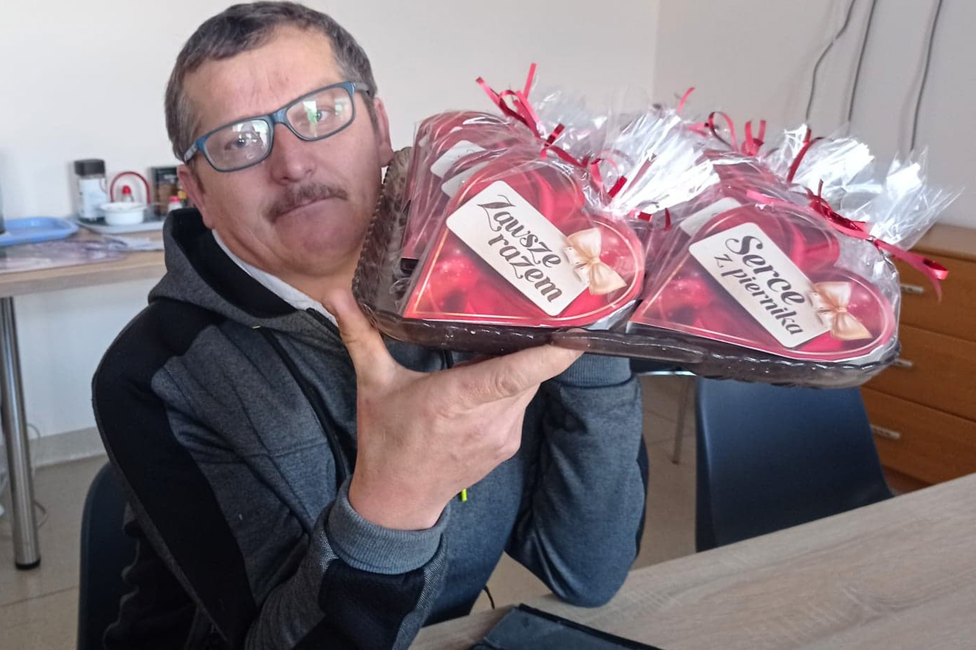 Mężczyzna w okularach trzyma na tacy kilka serc z piernika