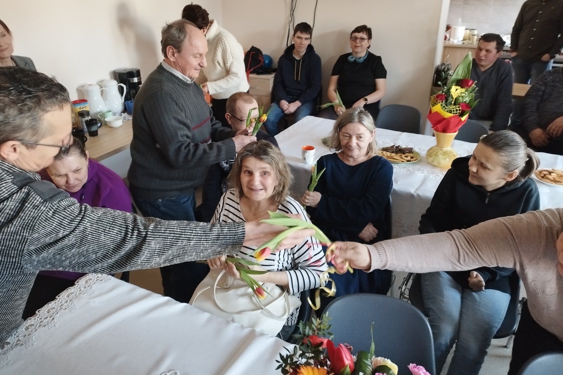 Panowie wręczają paniom kwiaty z okazji Dnia Kobiet