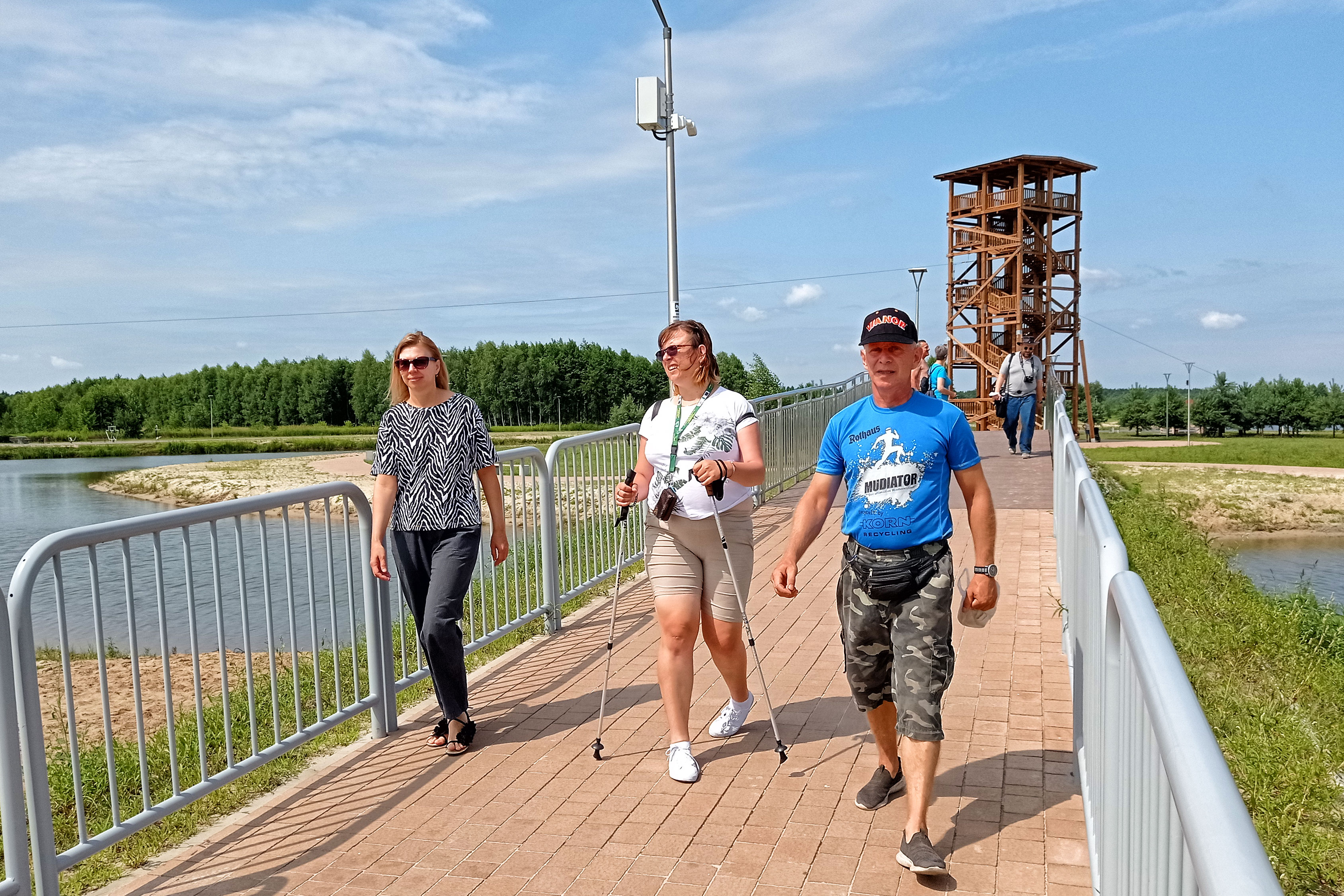Trzy osoby idą przez mostek. Na drugim planie wieża widokowa.