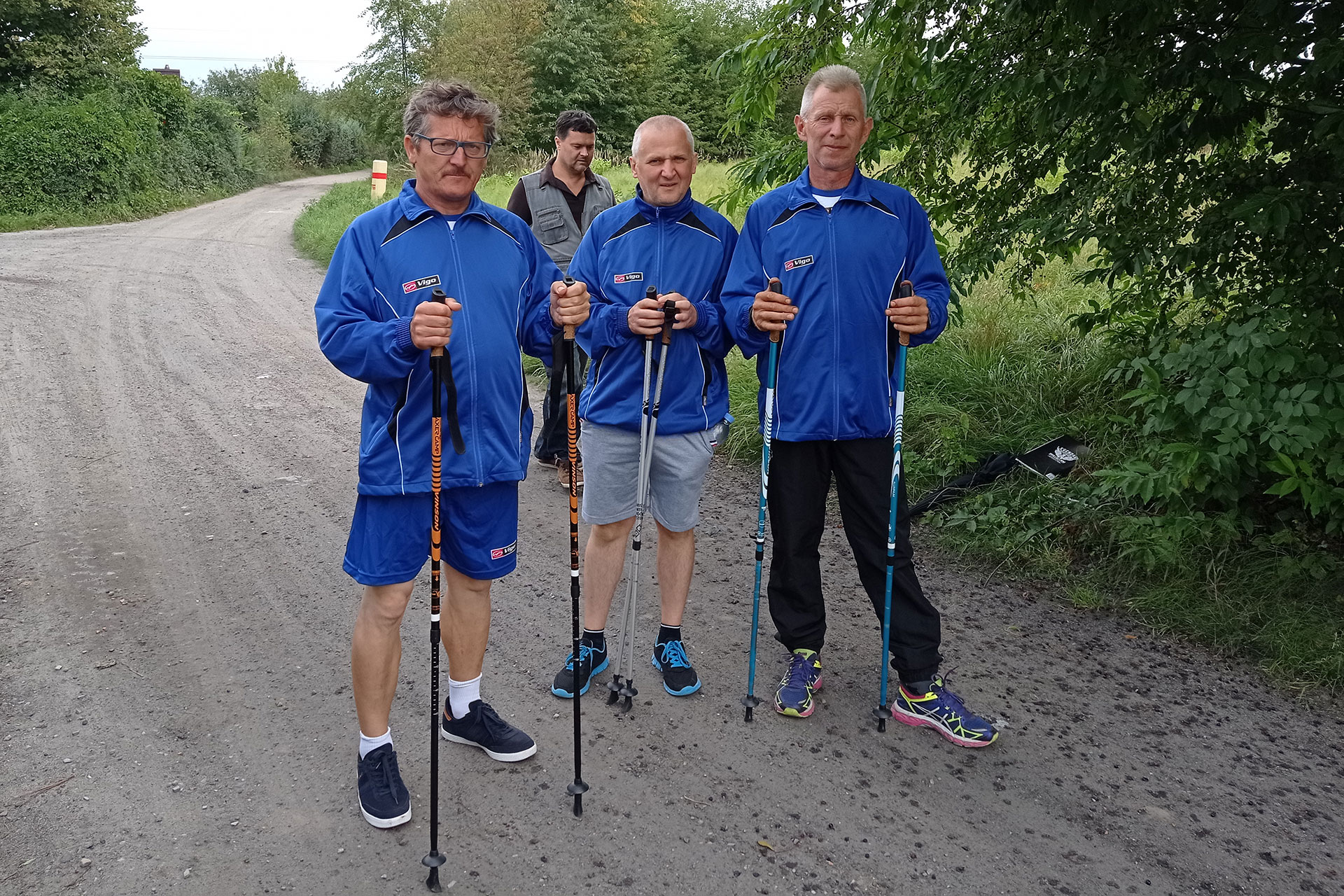 Trzech uczestników w strojach sportowych z kijkami Nordic Walking
